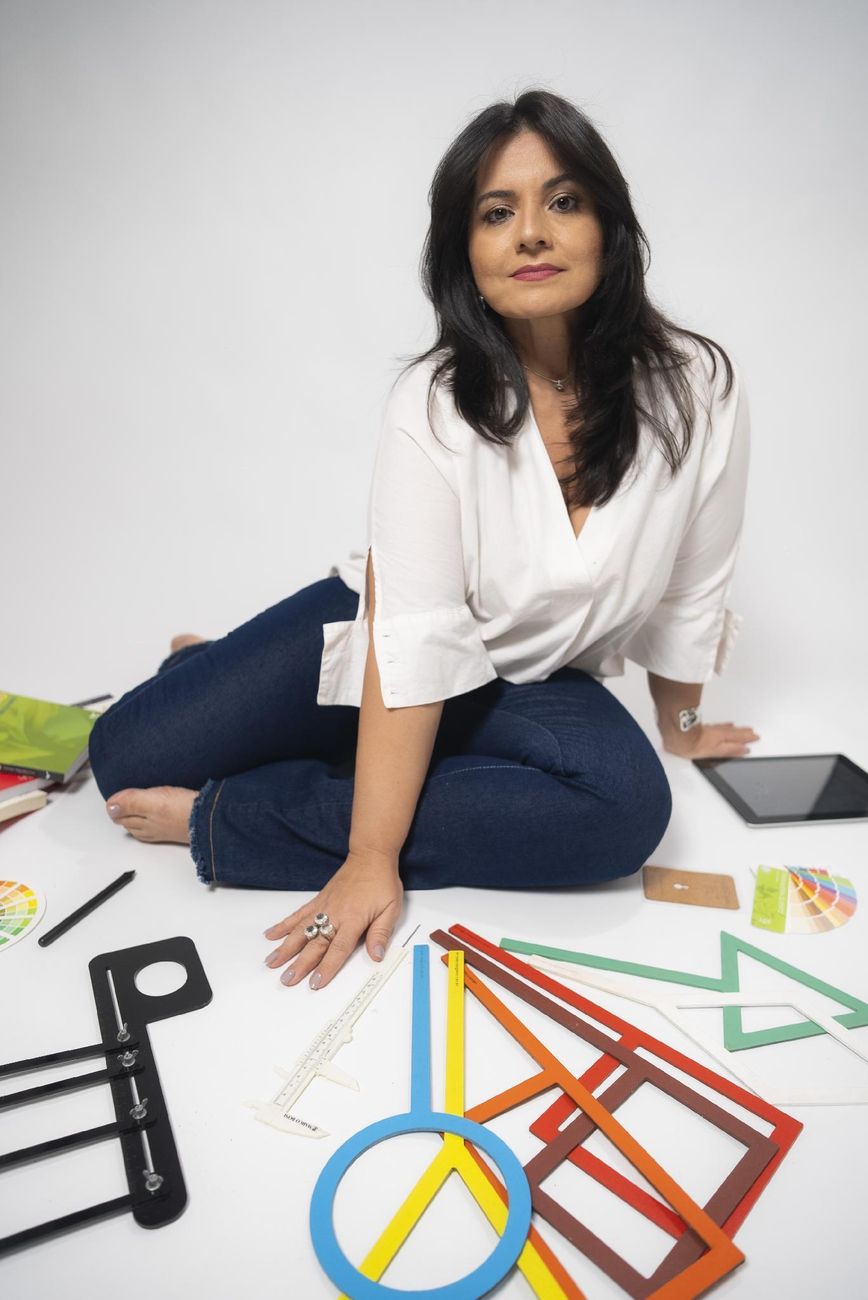 Carla Nascimento sentada no estúdio, entre formas geométricas e cartelas de cor